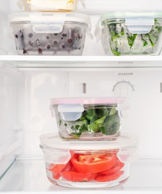 A close-up of the inside of a white fridge with four storage boxes with berries, greens, and tomatoes inside them