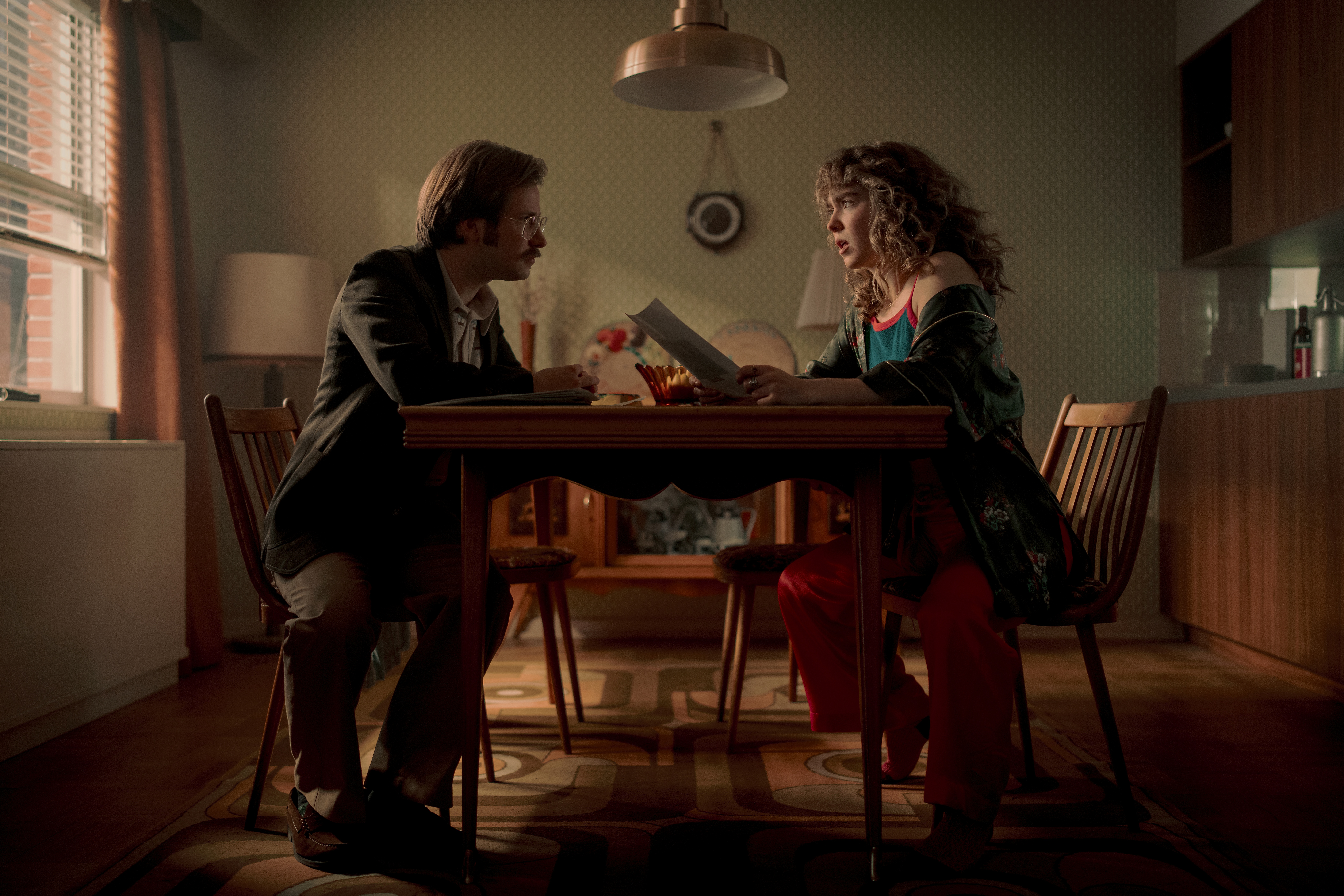 A series of film stills and photographs from a 1970s-inspired set featuring vibrantly decorated interiors with layered furniture and warm lighting, along with characters dressed in vintage clothing whether indoors or at parks, in cards, or at markets outdoors.