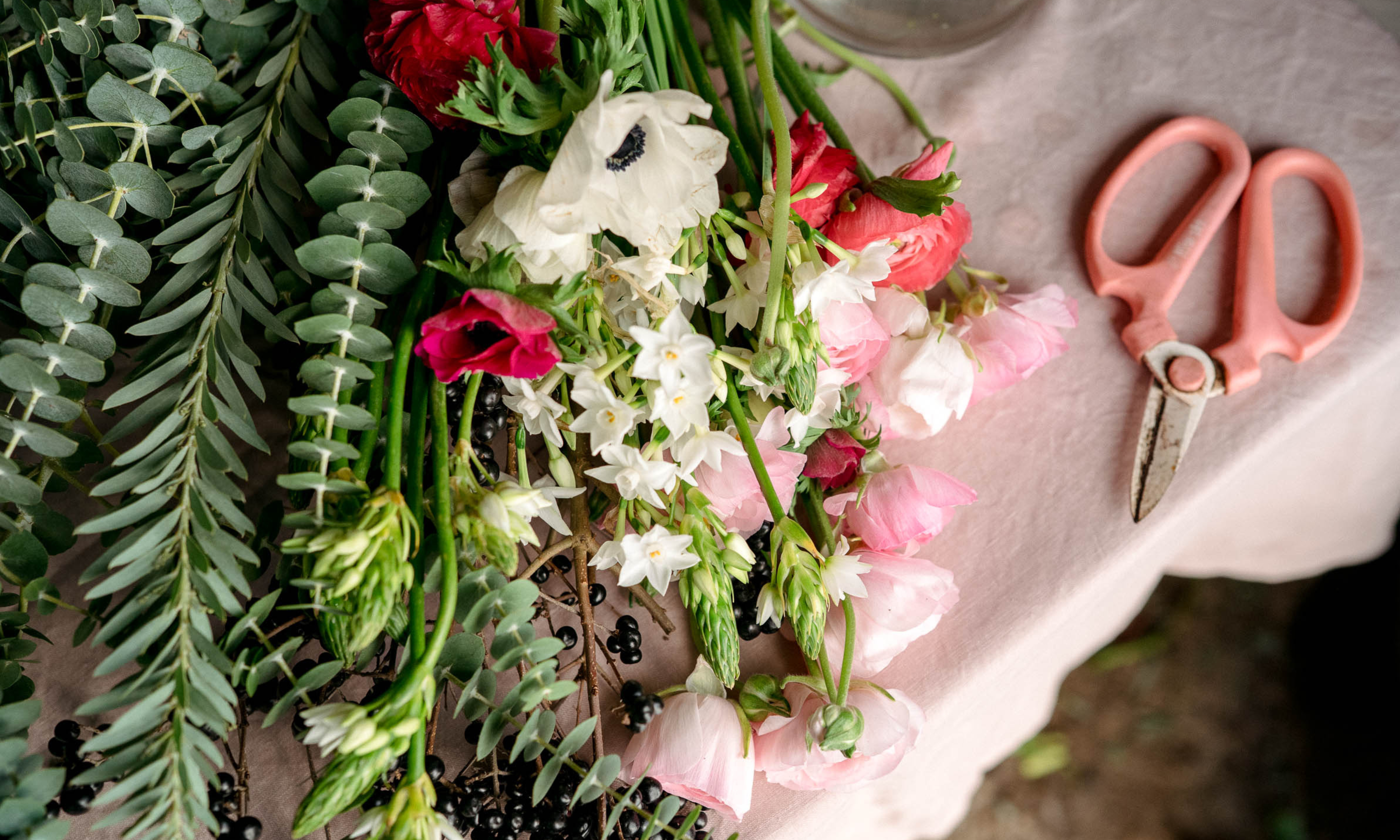Flower stems and pink scissors laid out on work bench