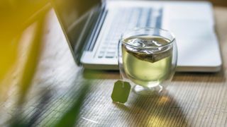 Glass mug of green tea sitting on desk with laptop