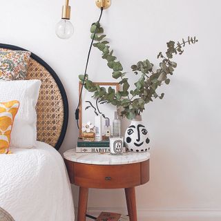 Kate Spiers bedroom with rattan headboard and mid century bedside table with eucalyptus on top.