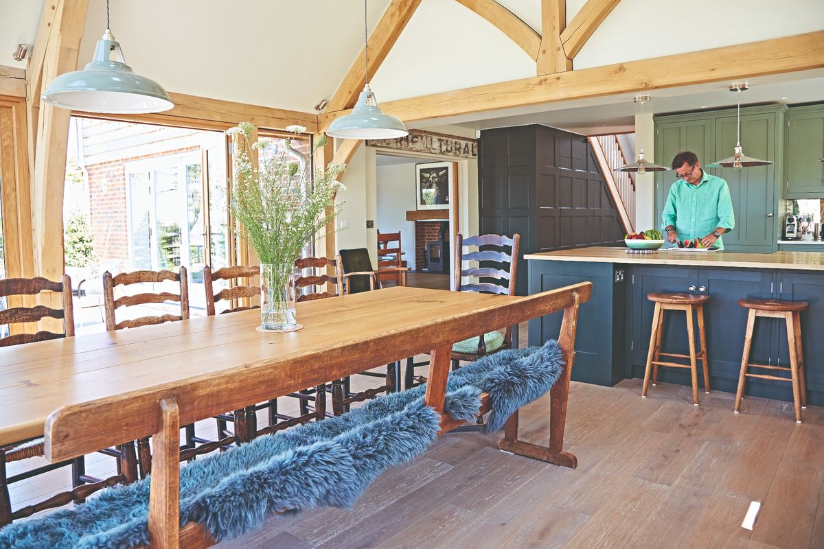 A man prepares a watermelon at a kitchen island in a kitchen-diner in an oak-framed extension