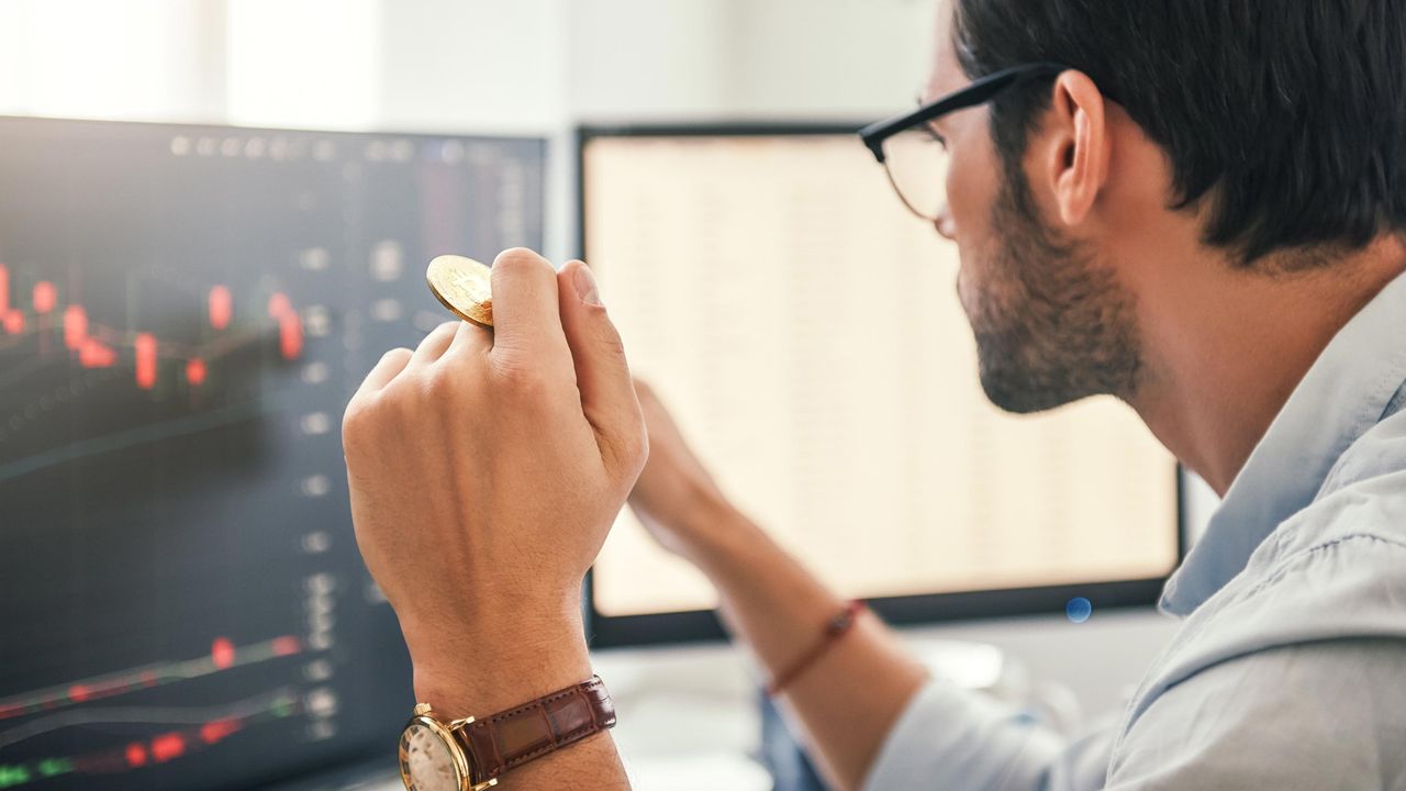 An investor holding a bitcoin looks at a computer screen.