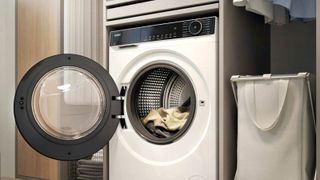 White washing machine in laundry room with door open, clothes inside and laundry basket next to it