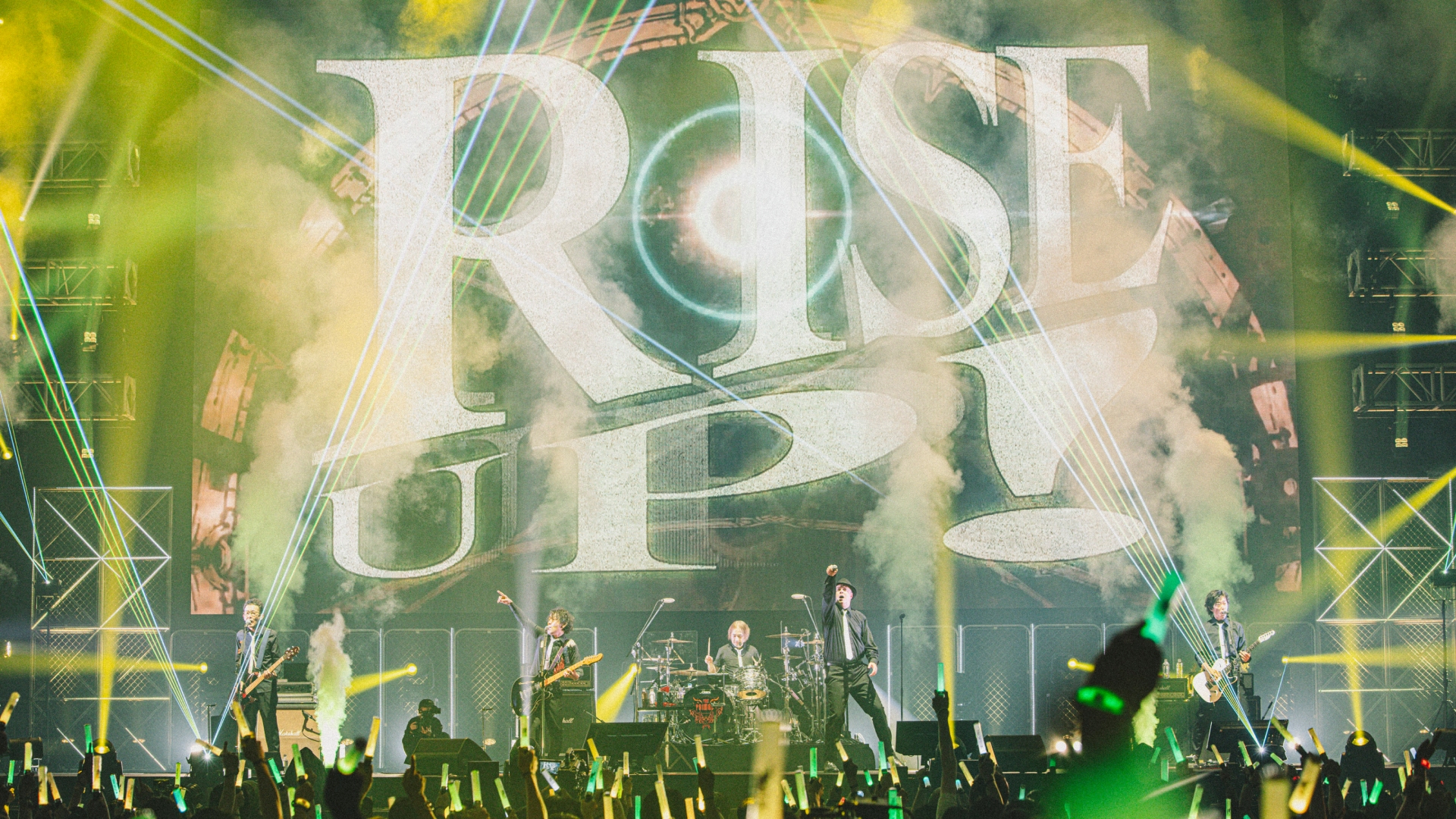 Final Fantasy 14 in-house band The Primals playing a concert, with the text 'Rise Up!' emblazoned in the background.