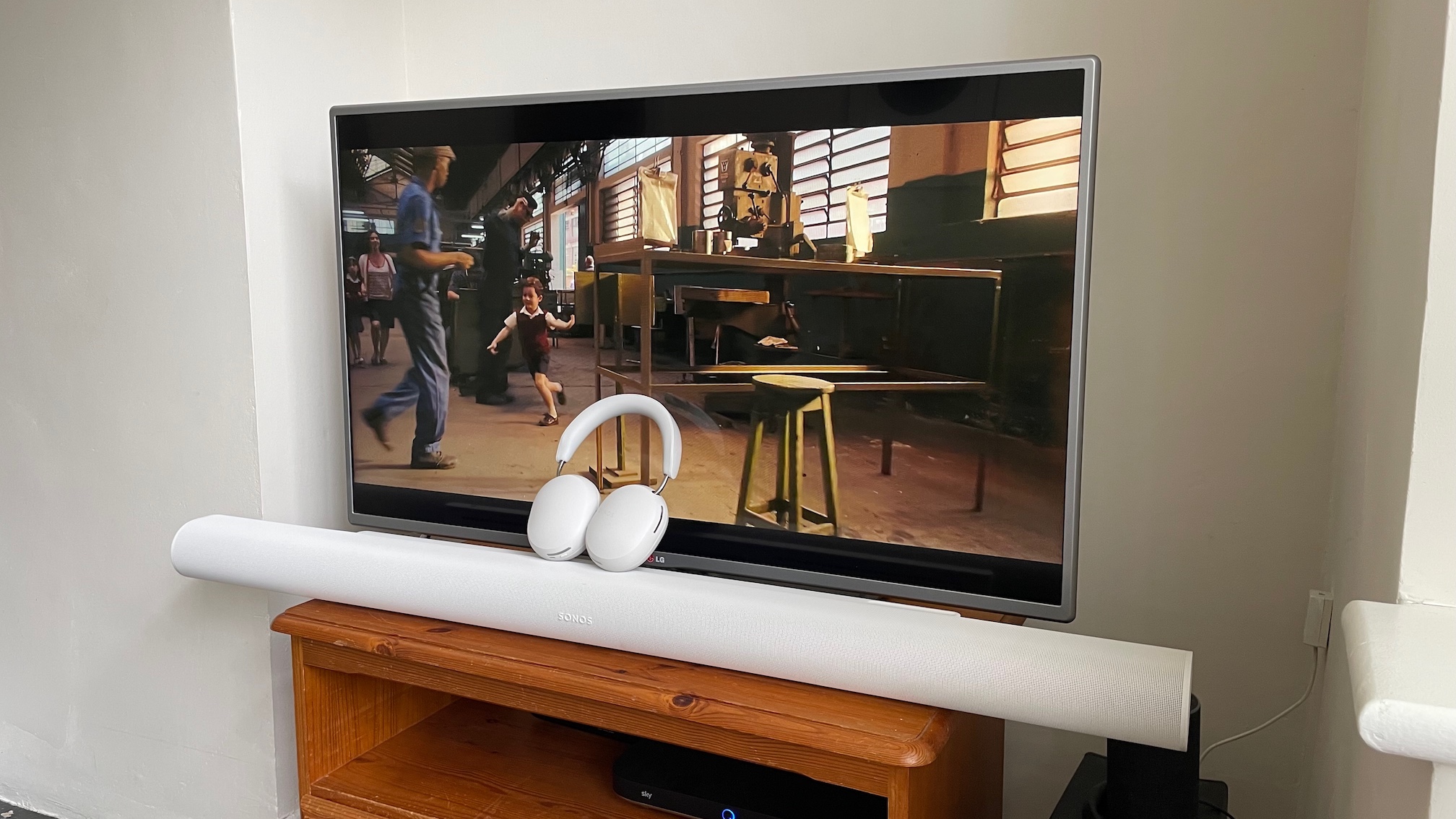 The Sonos Arc Ultra soundbar with Sonos Ace headphones placed on top of it, in front of a TV showing a scene from Senna on Netflix.