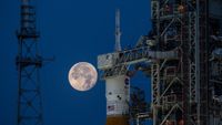 the full moon hangs in frame with the orion, inside its payload shell atop the SLS rocket.