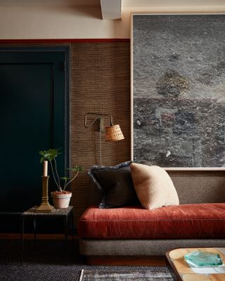 A living room with Benjamin Moore's Hale Navy painted on the door and trim with a large piece of art against a brown background and a brown and red sofa in front of it.