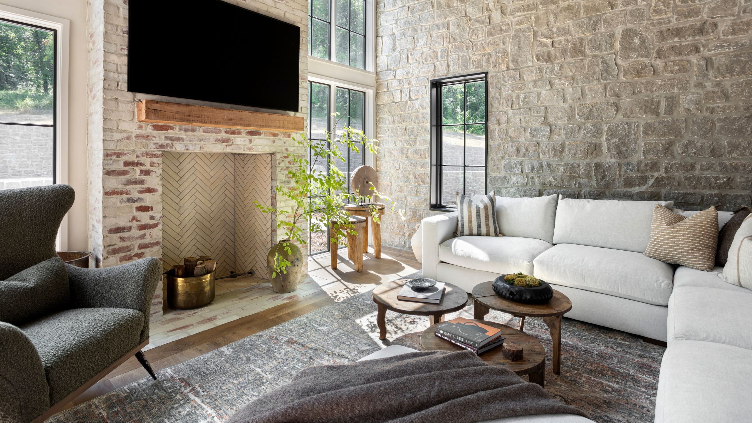 a large open living room with stone wall, glass windows and a brick fireplace with large white sectional
