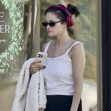 Selena Gomez was seen stepping out in Beverly Hills after a visit to Palm Beach Tan, sporting a relaxed yet stylish look. The singer and actress wore a white tank top, black sweatpants, and beige fuzzy slippers, accessorized with a cream-colored faux fur coat and pink headphones.