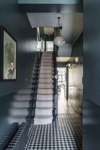 hall/entryway with small graphic black and white tiles, inky blue walls and painted stairs, stair runner