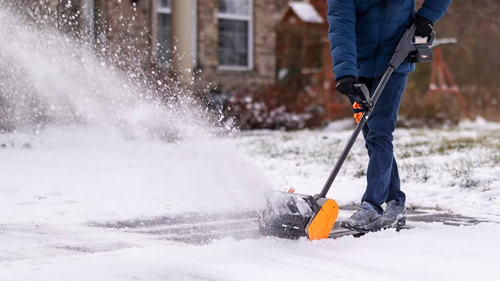 Man wearing blue coat and jeans used Wen cordless show shovel in front of house