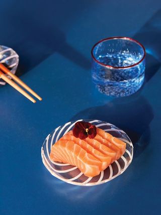 a clear glass plate with a line spiral design and slices of raw sushi and an edible flower on top