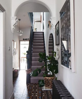A hallway with arched detail, black tiled flooring, black staircase with dark grey staircase runner and round mirror adjacent