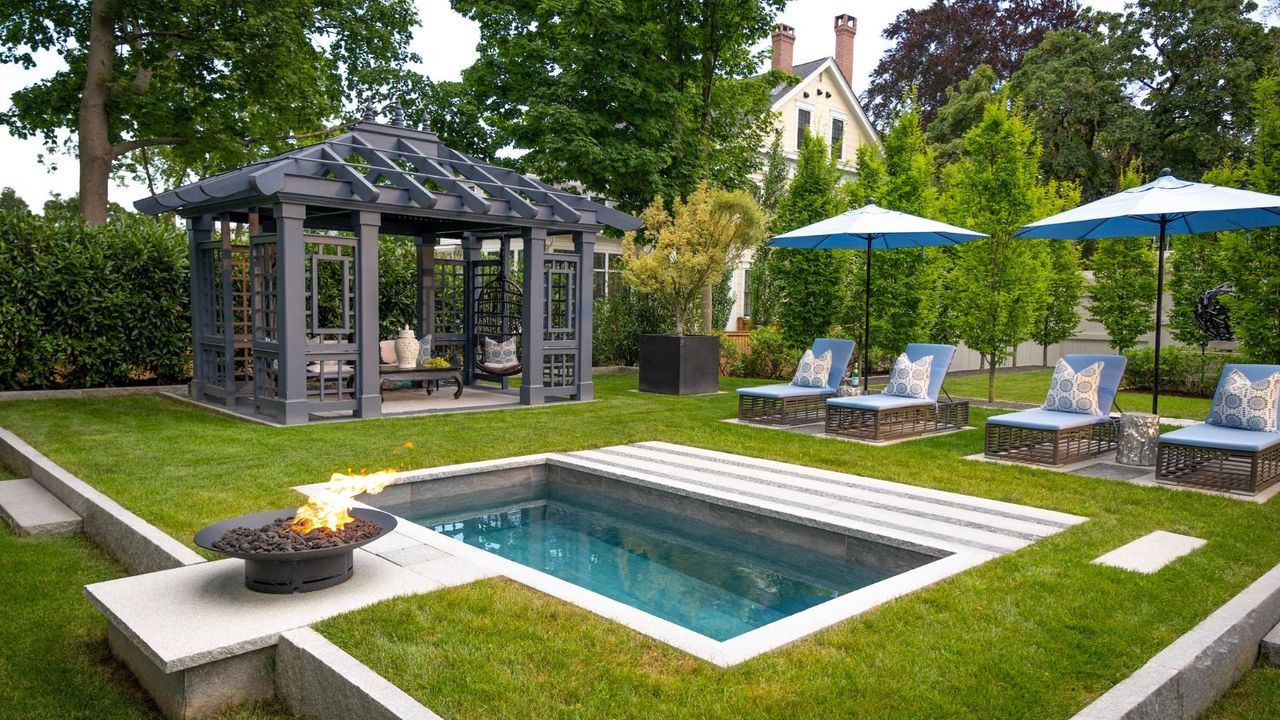 A plunge pool in a back yard with a summer house and summer pool loungers