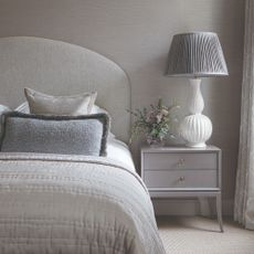 Grey bedding on double bed with bedside table and white vase in front of grey wall
