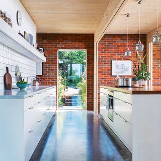 White galley kitchen with exposed brick wall and wooden ceiling