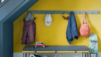 Understairs storage with yellow pegboard wallpaper and peg rail and bench