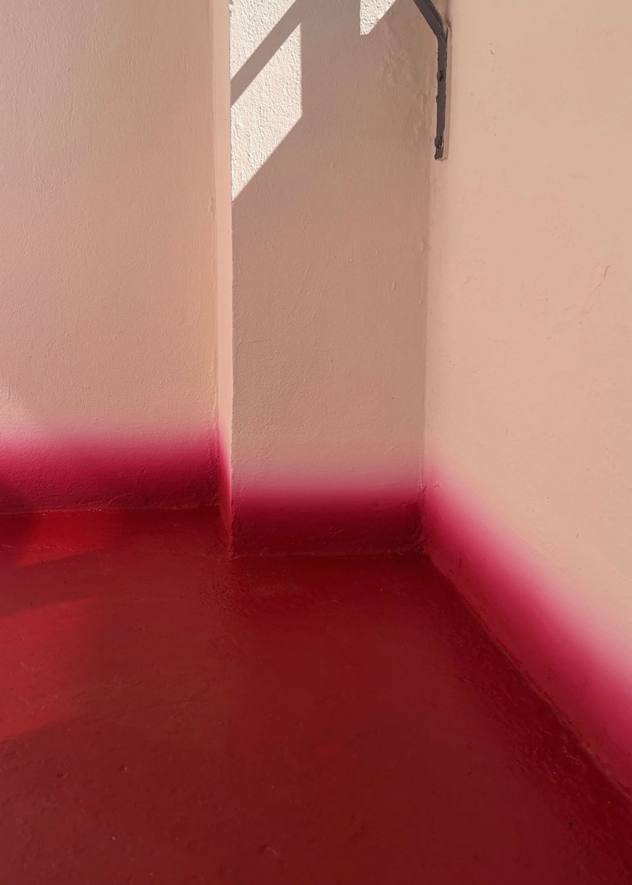The corner of a balcony that has white walls and a red floor with a gradient skirting board