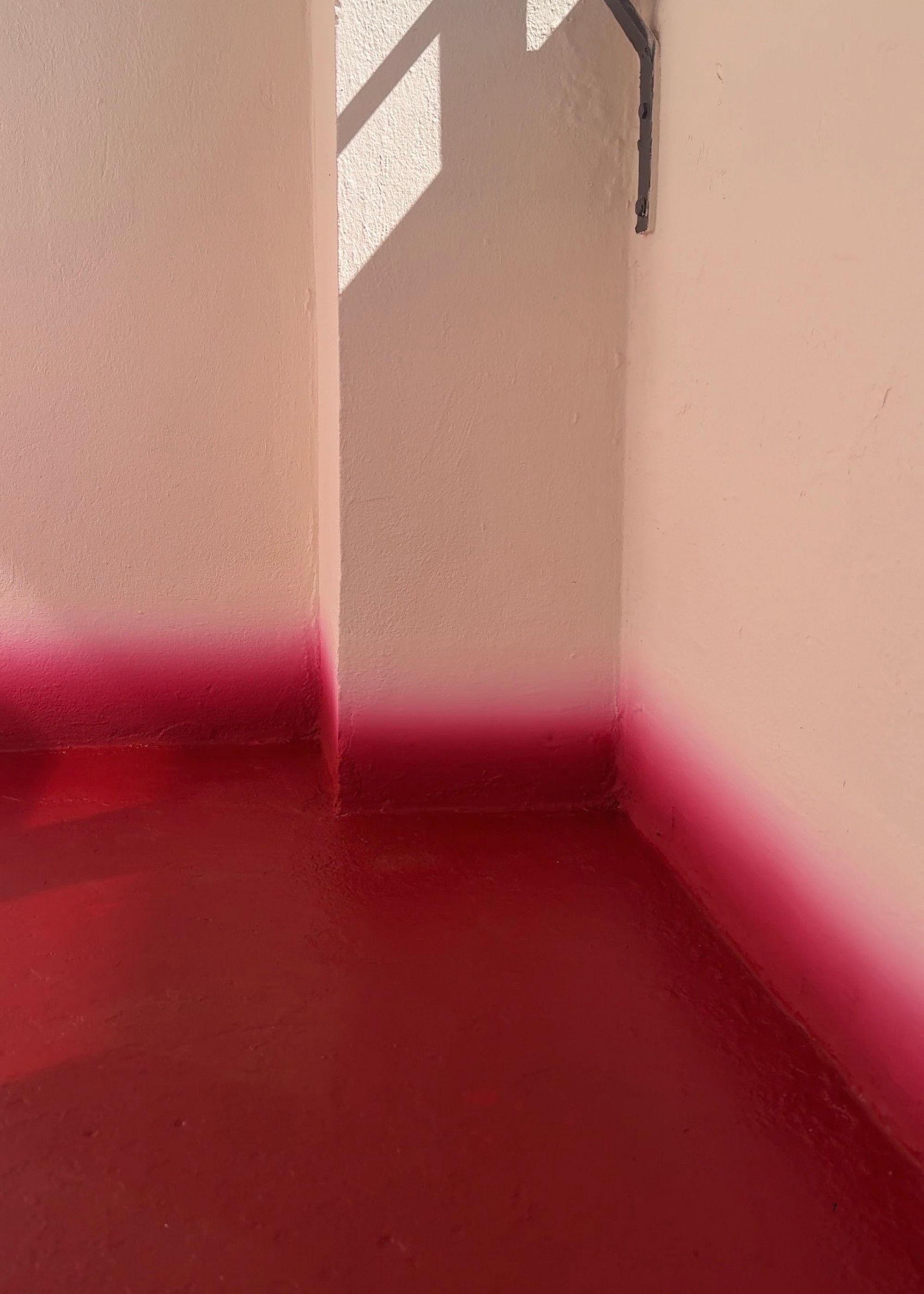 The corner of a balcony that has white walls and a red floor with a gradient skirting board