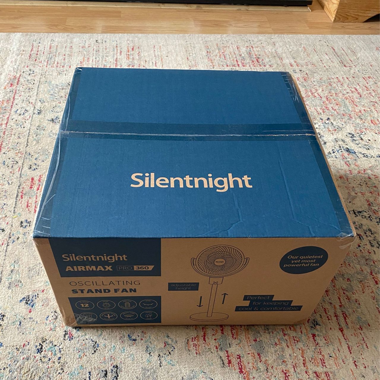 The cardboard outer packaging of the Silentnight Airmax Pro360 Pedestal Fan on a patterned rug