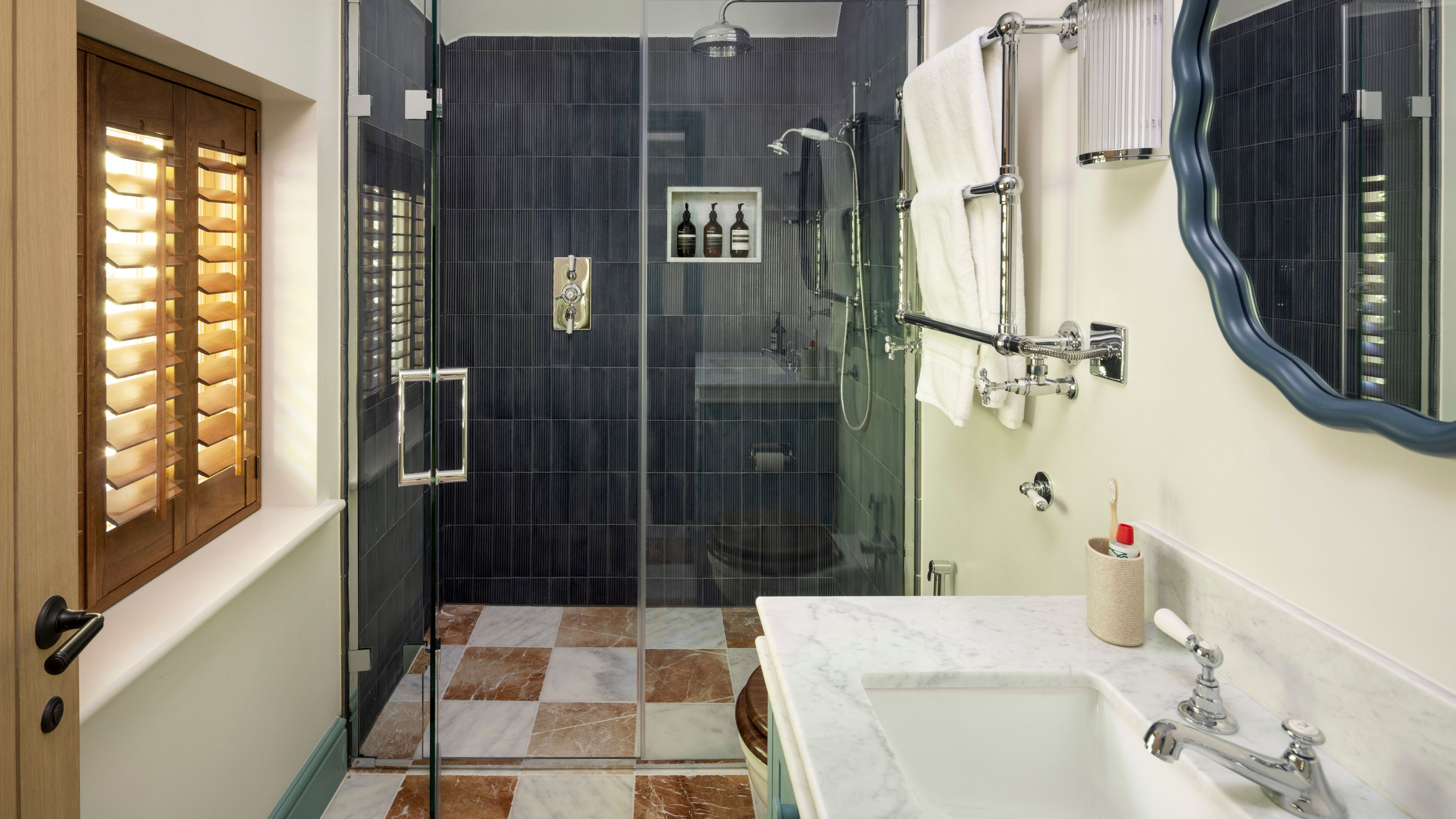 a loft bathroom with navy tiles in the shower, white and red checkerboard marble floor tiles, and a green painted vanity