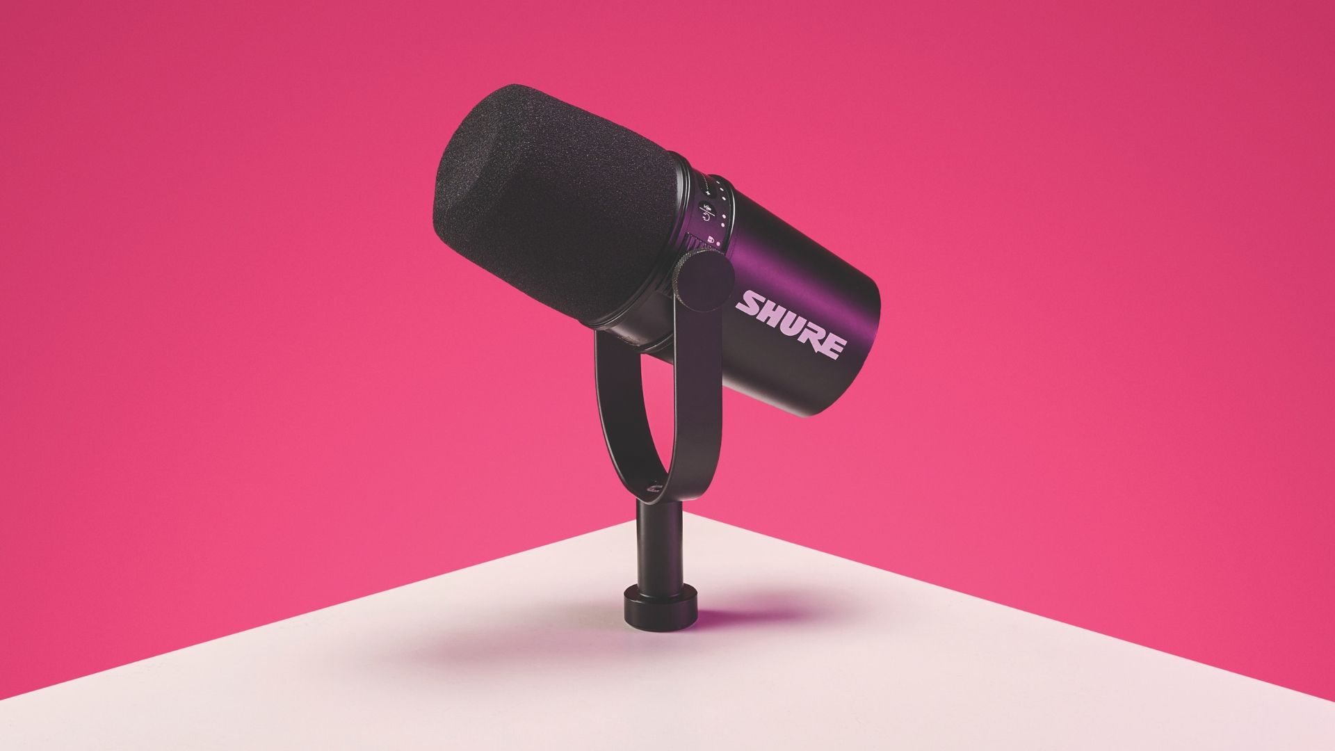 A Shure MV7 podcast mic on a table with a pink background