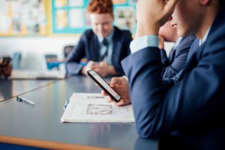 A schoolboy on his phone while sat at a desk