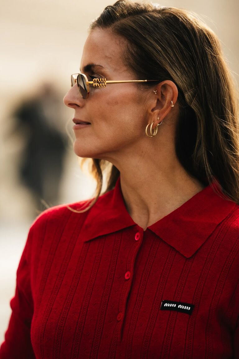 a woman wearing a red Miu Miu polo sweater and gold sunglasses at paris fashion week