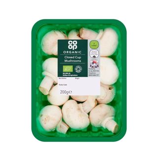 Green punnet of closed cup mushrooms surrounded by plastic wrap and with a label on the top