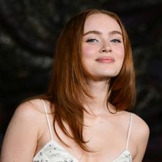 a close up photo of a white women with long, red hair posing on a red carpet