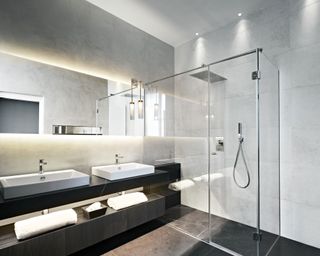 A glass shower next to a double vanity unit with LED mirror lights