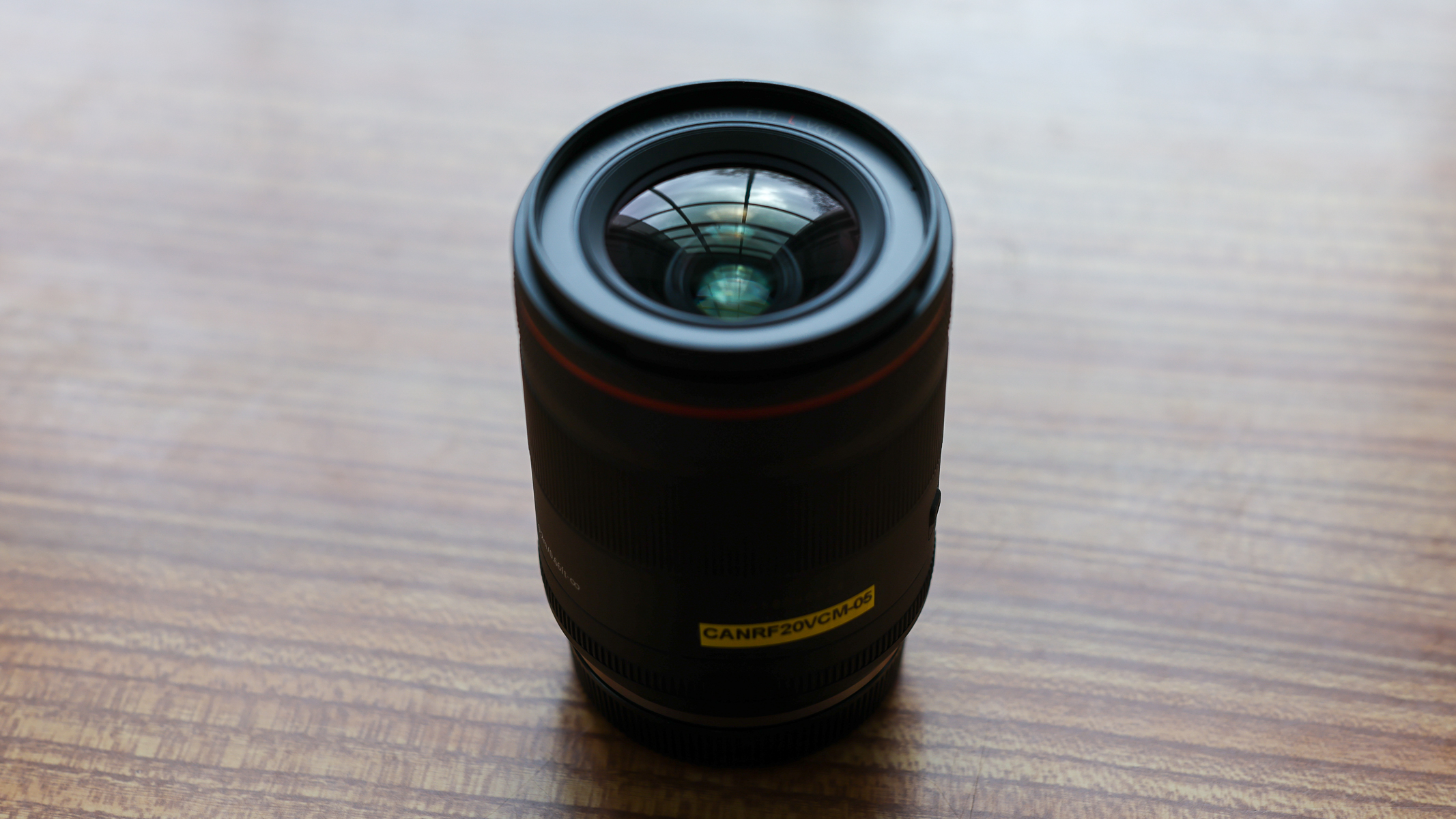 A Canon RF 20mm f/1.4 L VCM lens on a wooden table.