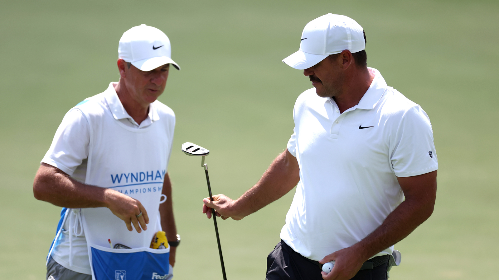 Brooks Koepka hands his caddie his putter