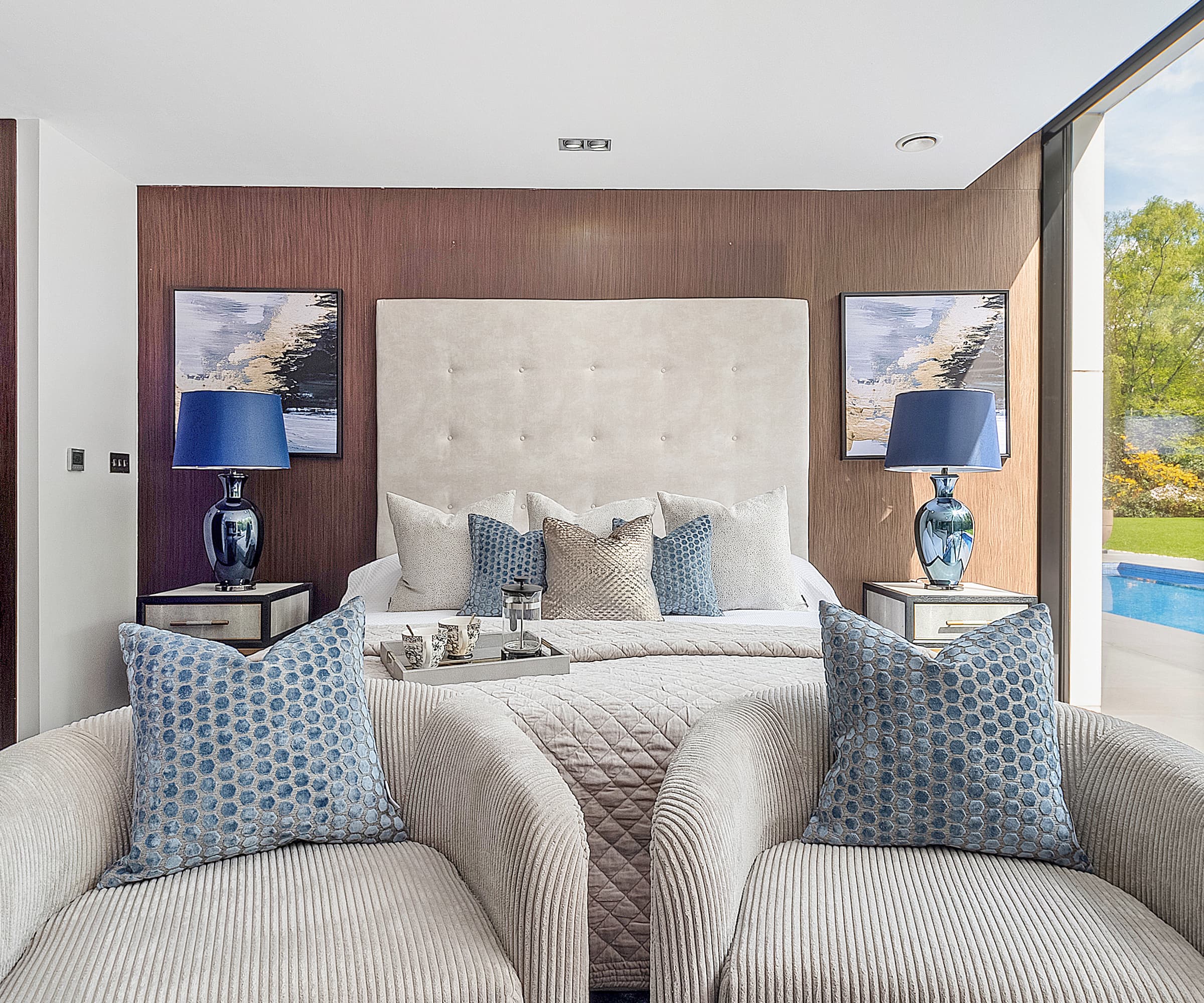 A master bedroom with two beige chairs at the end of the bed