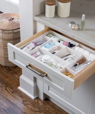 Open white shaker style bathroom drawer with dividers to organize toiletries and cosmetics