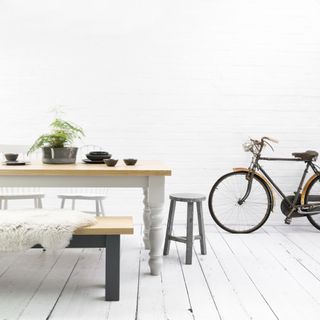 a white space with wooden grey painted dining table, stools and bench a bike is in the background