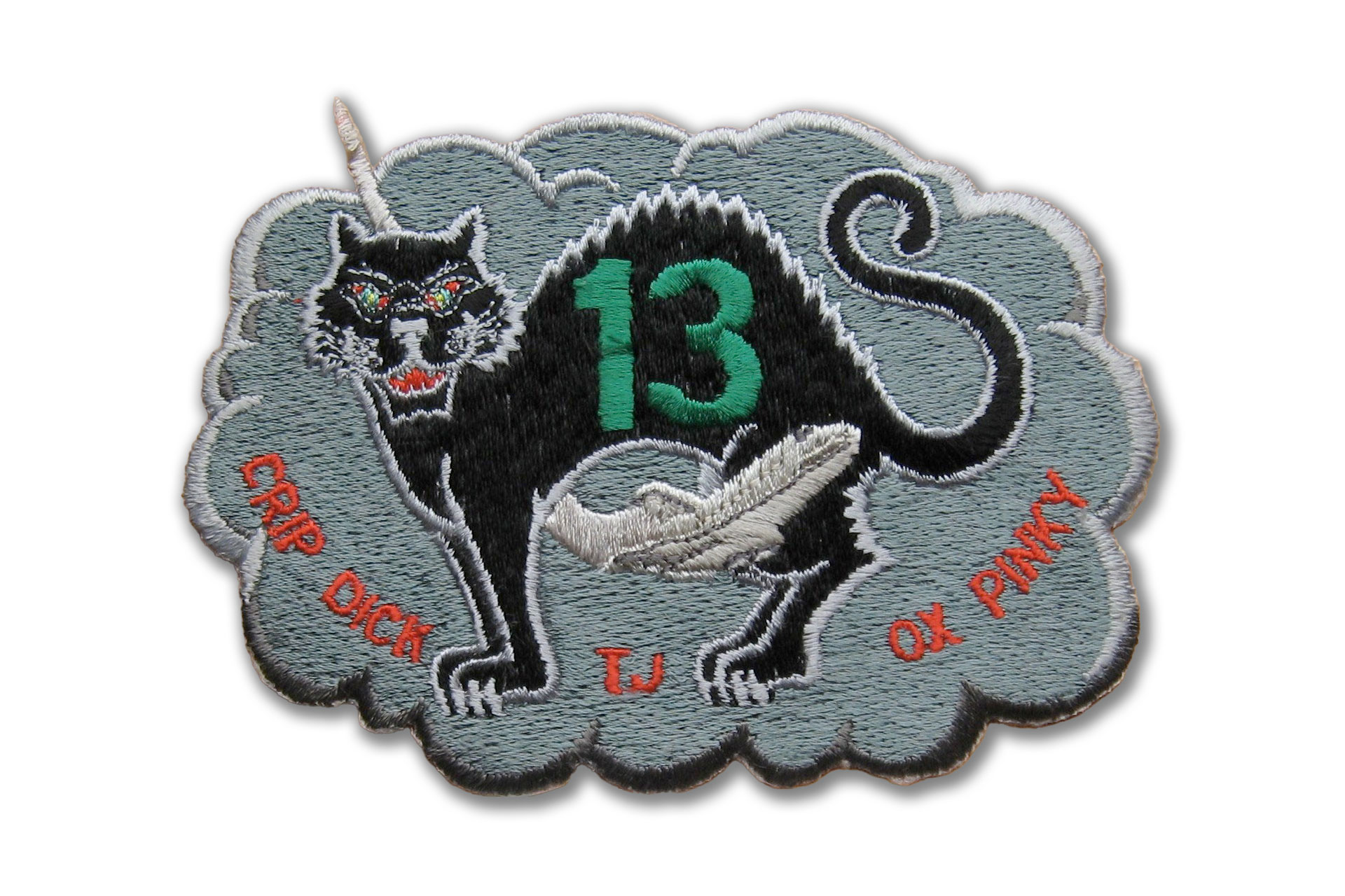 An embroidered emblem in the shape of a grey cloud with a black cat at its center. On the cat is written the arabic numeral "13" and a shuttle is soaring between its legs.