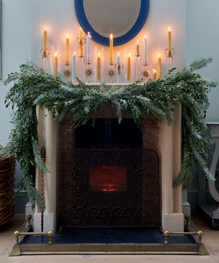 stone fireplace decorated for christmas with a huge garland and lots of taper candles