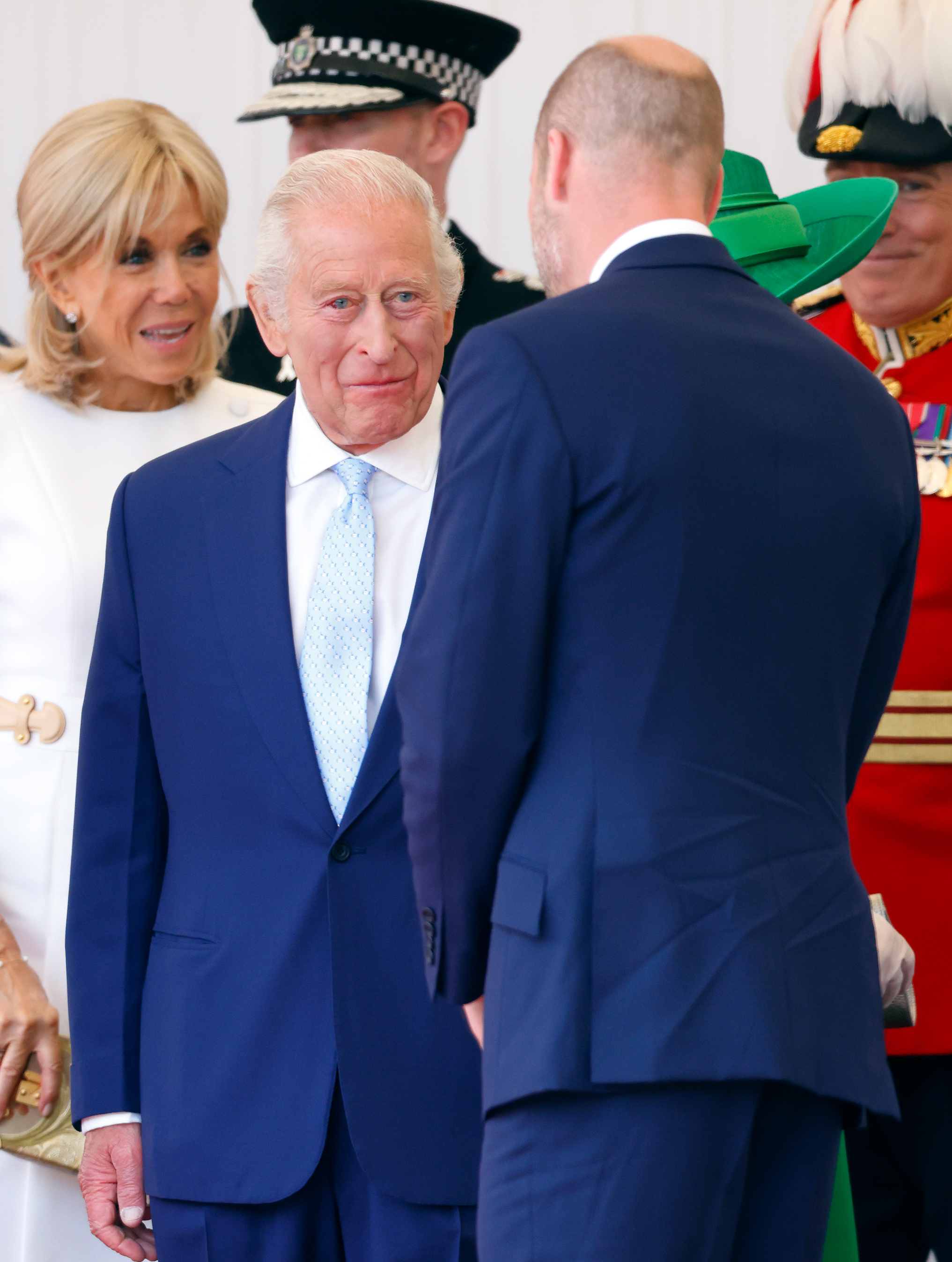 King Charles talking to Prince William, whose back is to the camera. Both are wearing similar navy suits