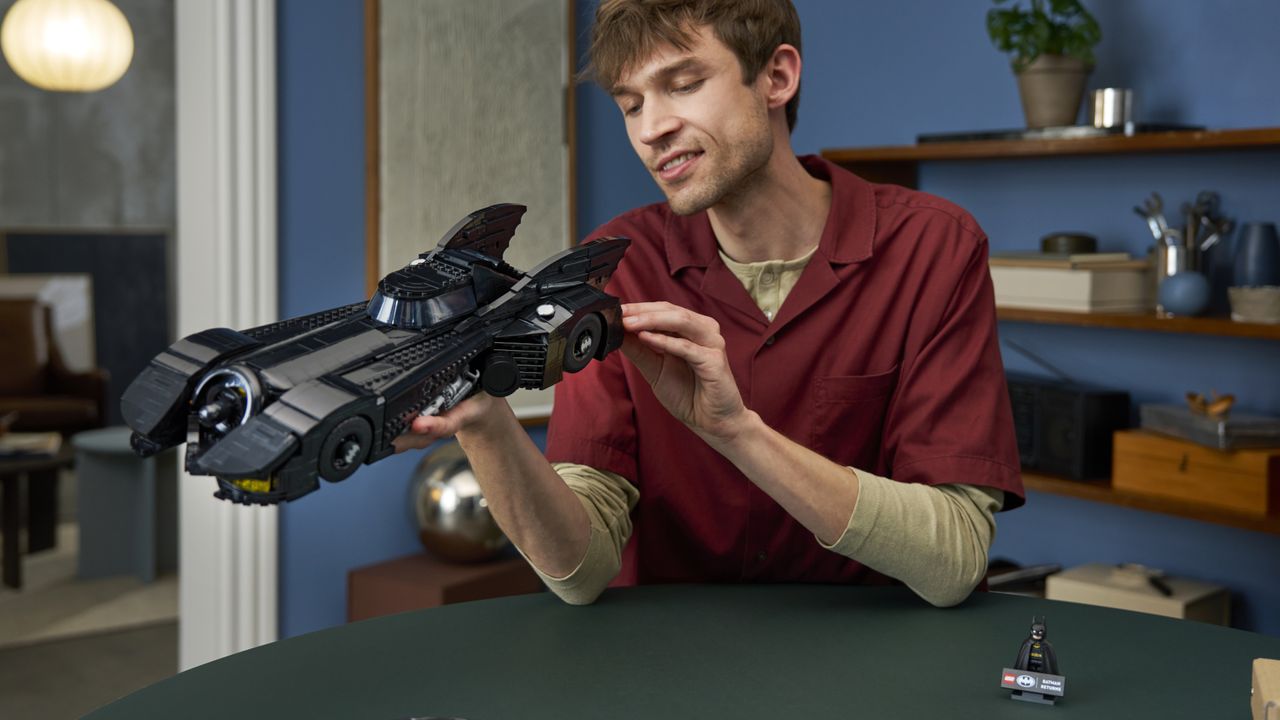 A man smiles while holding the Lego Batman Returns Batmobile