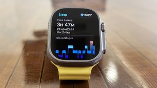 Apple Watch Ultra med tidtaking og gul rem på et trebord.