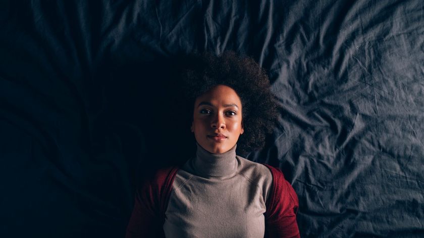 A woman lying on her back in bed, on top of the covers, staring straight ahead