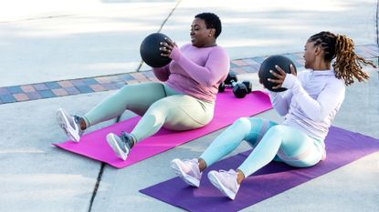 Two women doing Russian twists with medicine balls.