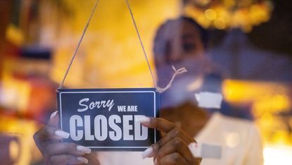 Woman puts a 'We're closed' sign on door of shop.