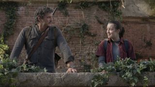 Pedro Pascal as Joel and Bella Ramsey as Ellie smile on a balcony in a post-apocalyptic setting in The Last of Us, season 1