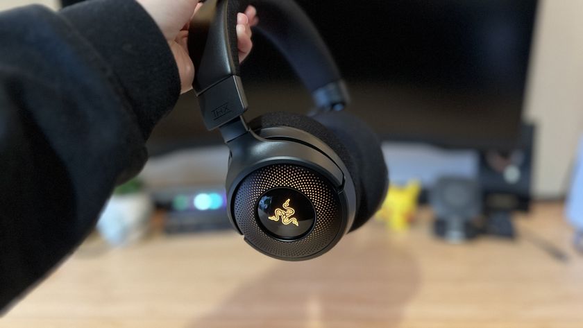 Hand holding Razer Kraken V4 headset against a PC setup