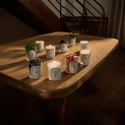 Diptyque's 5 new scented candles on a wooden table next to a staircase