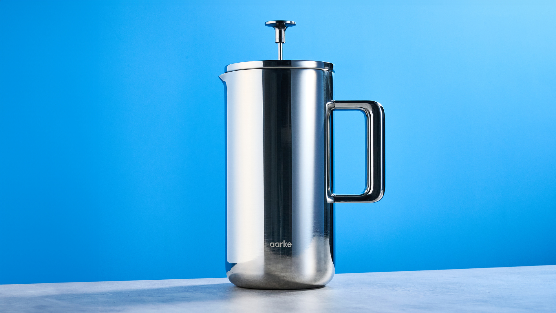 the aarke french press in silver showing the french press filter system, lid, spout, and inside photographed against the blue tom's guide background