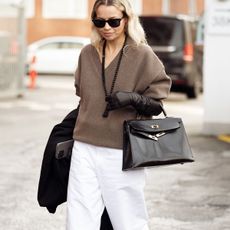 Woman in beige sweater, white jeans, and necklace